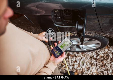Hochwinkelansicht des Menschen, der Elektroauto auflädt, Ladeanwendung prüfen. Stockfoto