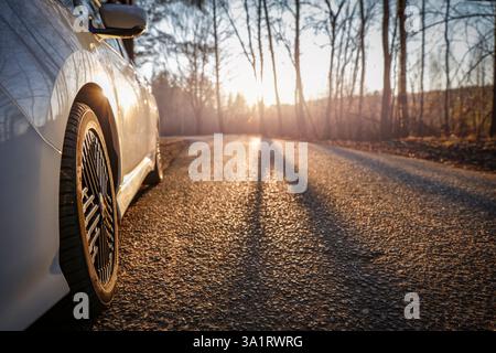 Flacher Winkel eines weißen Autos, das auf der Seite der asphaltierten Straße geparkt ist, die sich durch den Wald schlängelt. Sonnenlicht und Schatten von hohen Bäumen. Stockfoto