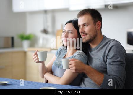 Ein interrassisches Paar trinkt Kaffee und blickt weg in der Küche eines Hauses Stockfoto