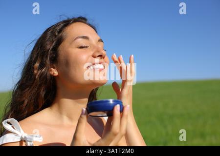 Happy Woman hydratisiert Sking mit Feuchtigkeitscreme auf einem grünen Feld an einem sonnigen Tag Stockfoto