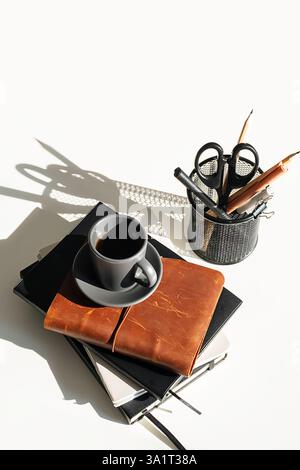 Bücherstapel, Schreibwaren und Espresso-Kaffeetasse auf weißem Schreibtisch. Stockfoto