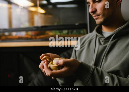 Fröhlicher Haustierbesitzer, der eine Albino-Kugel-Python in der Nähe seines Lebensraums hält Stockfoto
