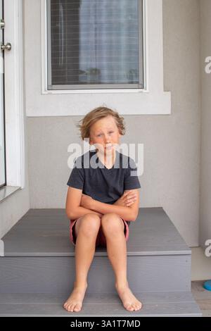 Der Junge sitzt im Sommer barfuß auf der Veranda Stockfoto
