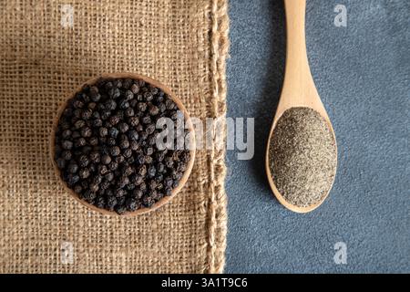 Gemahlener schwarzer Pfeffer mit Körnern schwarzen Pfeffers auf grauem Hintergrund Stockfoto
