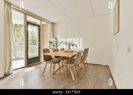 Ein stilvoller Essbereich mit einem Holztisch und grauen Stühlen, von großen Fenstern in sanftes Tageslicht getaucht, mit einem ruhigen Blick auf den Außenbereich. Stockfoto