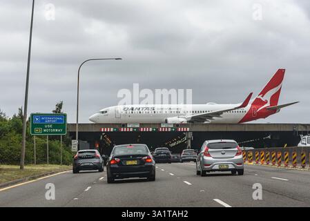 Eine Qantas Boeing 737-800 (VH-XZE), die auf der Landebahn am Sydney Kingsford Smith Airport fährt, die über die Autobahn M1/M5 führt Stockfoto