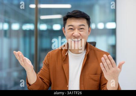Webcam-Ansicht, erfolgreicher asiatischer Mann, der die Kamera lächelt und mit Kollegen und Partnern kommuniziert. Online-Geschäftstreffen, Konferenzpräsentation, Geschäftsmann sitzt im Büro Stockfoto