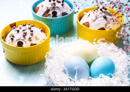 Köstliche Ostercupcakes und Eier auf hellblauem Hintergrund mit Blumen. Osterkuchen mit Glasur in hellen Backformen in Gelb- und Himmelsfarbe. Hallo Stockfoto