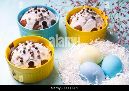 Köstliche Ostercupcakes und Eier auf hellblauem Hintergrund mit Blumen. Osterkuchen mit Glasur in hellen Backformen in Gelb- und Himmelsfarbe. Hallo Stockfoto