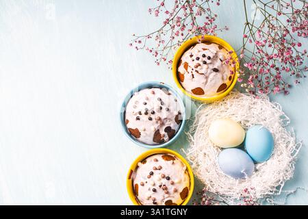 Köstliche Ostercupcakes und Eier auf hellblauem Hintergrund mit Blumen. Osterkuchen mit Glasur in hellen Backformen in Gelb- und Himmelsfarbe. Co Stockfoto