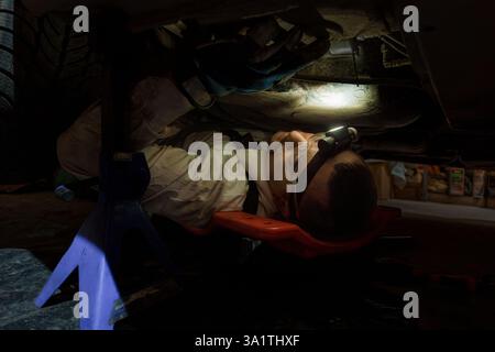 Mechaniker, der den Scheinwerfer trägt, sorgfältig die Unterseite des Fahrzeugs in der Autoreparaturwerkstatt überprüfen. Stockfoto