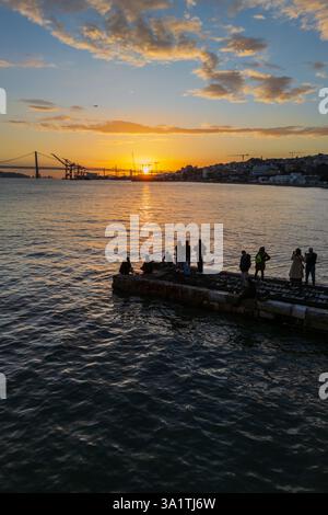 Aus der Vogelperspektive sehen Sie die Menschen, die den Sonnenuntergang von einem Dock am Ufer des Cais do Sodre genießen, einem pulsierenden Nachtleben und einem Restaurantziel in Lissabon, Portugal Stockfoto