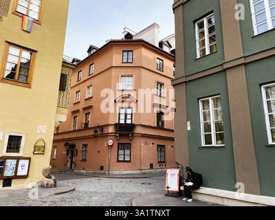 Warschau, Polen - 9. März 2025: Eine malerische Szene mit bunten Gebäuden in einer ruhigen Stadtstraße in Warschau. Mann sitzt am Telefon. Stockfoto