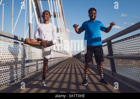 Zwei afroamerikanische Freunde trainieren auf der Brücke in der Stadt. Sie wärmen sich zum Joggen auf. Stockfoto