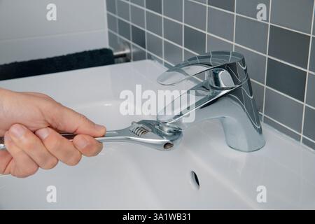 Nahaufnahme eines Mannes, der einen Schraubenschlüssel benutzt, um den Belüfter aus einem Waschbecken-Wasserhahn in einem Badezimmer zu entfernen Stockfoto