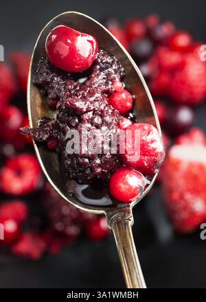 Das Foto zeigt eine Nahaufnahme eines Metalllöffels, gefüllt mit einer Mischung aus Beeren, einschließlich Kirschen, Brombeeren und Himbeeren. Stockfoto