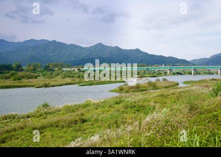 Namwon City, Südkorea - 3. Oktober 2021: Der Seomjin River schlängelt sich durch üppige Feuchtgebiete, mit einer grünen Brücke, die sich über das Wasser und die Wälder erstreckt Stockfoto