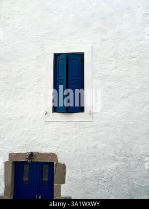 Eine weiß getünchte Wand mit leuchtend blauen Fensterläden und einer blauen Tür. Stockfoto