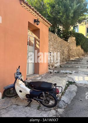 Ein alter Roller lehnt sich an ein Terrakotta-Haus in einer charmanten Gasse Stockfoto