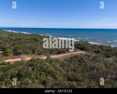 Kurvige Straßenkurven durch dichte grüne Landschaft treffen auf das Meer unter hellblauem Himmel. Stockfoto