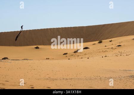 Silhouette eines einsamen Mannes, der auf dem Kamm einer Sanddüne in der Sosssusvlei-Region des Namib-Sandmeers in Namibia spaziert. Stockfoto