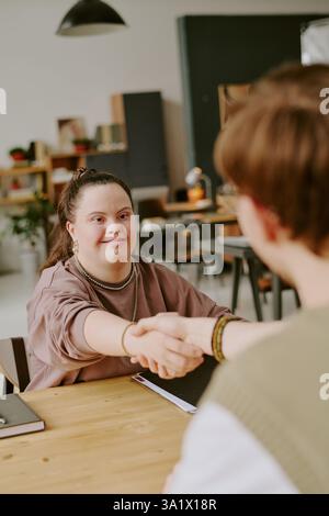 Vertikalaufnahme eines jungen Bewerbers mit Down-Syndrom beim Händeschütteln mit männlichem Interviewer Stockfoto