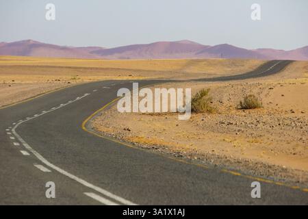 Die Teerstraße in Richtung Sossusvlei führt durch die raue und einsame namibische Landschaft mit den hohen roten Dünen der Namib-Wüste, die sich in der d erheben Stockfoto