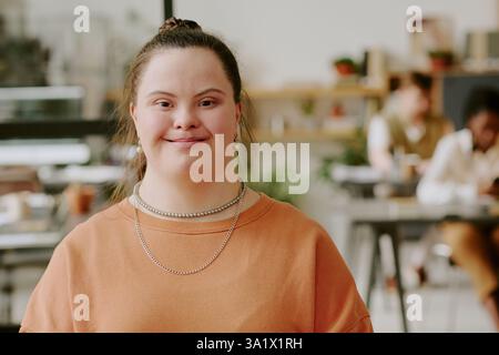Mittelgroßes Nahporträt einer glücklichen Büroangestellten mit Down-Syndrom, die sich im modernen Büro zum Foto posiert Stockfoto