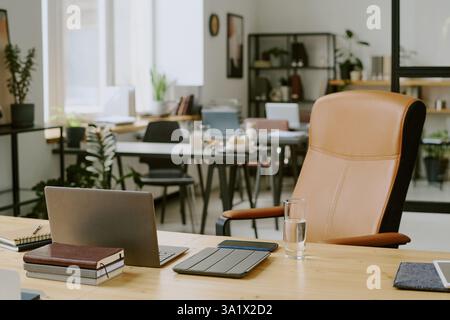 Holzschreibtisch mit Laptop und Büroartikeln auf der Oberseite und beigefarbener Ledercomputerstuhl im modernen Büro Stockfoto