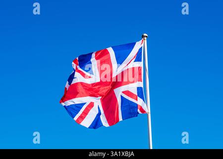 Union Jack Flagge auf einem Fahnenmast, Union Flag winkt gegen einen blauen Himmel Stockfoto