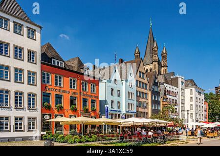Cafés im Freien unter den farbenfrohen Häusern des Kölner Fischmarktes, mit der imposanten Martinskirche im Hintergrund. Köln, Deutschland Stockfoto
