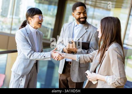 Drei Profis in stilvoller Geschäftskleidung teilen sich einen freundlichen Handschlag, während sie in einer hellen, modernen Büroumgebung mit Cit Ideen diskutieren Stockfoto