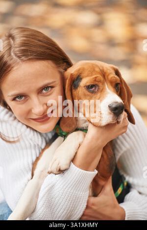 Sitzend, mit einem Tier in der Hand und in die Kamera. Die junge Frau ist mit ihrem Hund im Park. Stockfoto