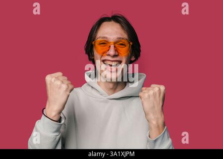 Ein freudiger junger Mann feiert aufgeregt, während er eine stilvolle Sonnenbrille mit Attitüde trägt Stockfoto