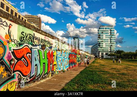 Farbenfrohe Graffiti auf dem East Side Gallery Abschnitt der Berliner Mauer mit Touristen, die die historische Stätte und Kunstwerke bewundern. Berlin Stockfoto