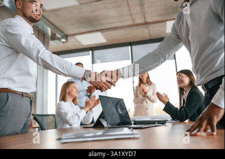 Nahaufnahme des Handshake. Erfolgreicher Deal. Eine Gruppe von Büroangestellten ist drinnen zusammen. Stockfoto