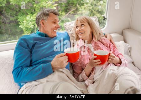 Ältere Ehepaare mit Tassen heißen Kaffee liegen im Bett in ihrem Campingfahrzeug Stockfoto