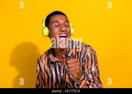 Energiegeladener junger Mann, der Musik mit Kopfhörern vor leuchtendem gelbem Hintergrund genießt Stockfoto