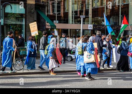 Ein Protest mit Menschen, die Schilder und Fahnen halten, einige tragen blaue Kleider, findet auf einer Stadtstraße statt, in der Polizeipräsidenz und Gebäude im Backgr Stockfoto
