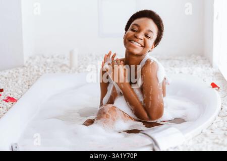 Frau mit geschlossenen Augen des Vergnügens Baden mit Schaum Und Blütenblätter zu Hause Stockfoto