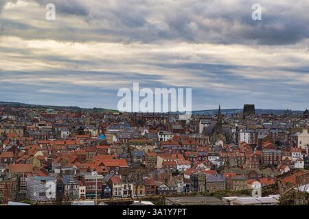 Ein Blick aus der Vogelperspektive zeigt ein dichtes Stadtbild mit roten Ziegeldächern unter einem bewölkten Himmel, unterbrochen von einem Kirchturm und einem Burgturm in Whitby, Großbritannien. Stockfoto