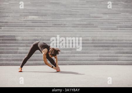 Dehnung nach dem Training. Afroamerikanische Frau mit Fitness-Tracker und kabellosen Kopfhörern macht Übungen für Beine Stockfoto