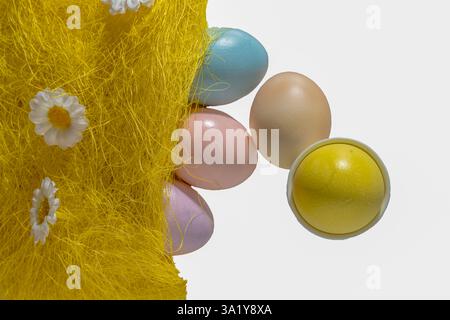 ostereier in Pastell, die aus einem gelben Strohbeutel Rollen. Ein Eierbecher auf weißem Marmorhintergrund. Flach, Kopierbereich. Stockfoto