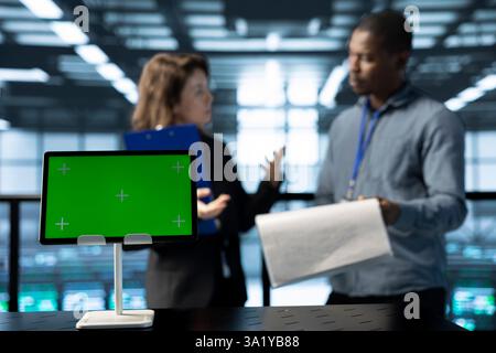 Konzentrieren Sie sich auf ein Modell-Tablet vor dem Prüfer des Rechenzentrums, der neben dem Manager die Papierkram überprüft. Nahaufnahme des Geräts mit isoliertem Bildschirm neben dem Supervisor, der die Dokumentation der Serverfarm überprüft Stockfoto