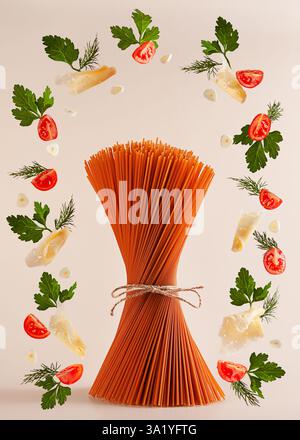 Roter Tomatenpasta, roh, steht auf dem Tisch, umgeben von Produkten, die umherfliegen: Tomaten, Käse, Knoblauch, Kräuter. Die Inhaltsstoffe werden auf einem p Stockfoto