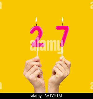 Geburtstagsnummer 27 - Hände halten fuchsiafarbene Kerzen Stockfoto