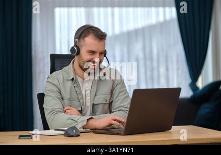 Ein glücklicher Mann, der im Heimbüro arbeitet, kabellose Kopfhörer trägt, einen Videoanruf mit Kunden auf einem Laptop führt, den Kundenservice betreibt oder uns mit dem Support in Verbindung setzt Stockfoto