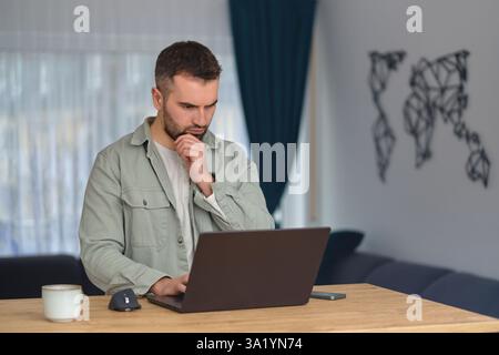 Ein junger Mann, der einen Laptop benutzt, während er im Heimbüro arbeitet. Stockfoto
