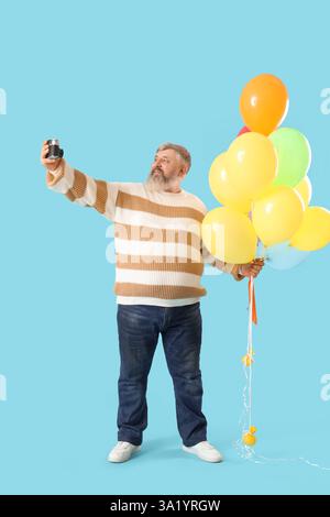 Senior Mann mit Ballons und Fotokamera, die Selfie auf blauem Hintergrund macht Stockfoto
