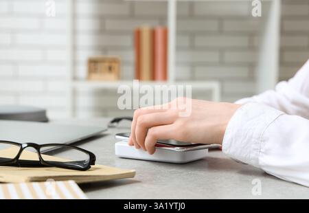Frau mit Mobiltelefon und kabellosem Ladegerät am Tisch im Büro Stockfoto